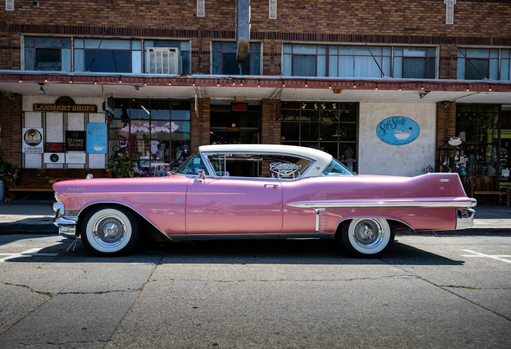 A pink classic car parks in front of a store.