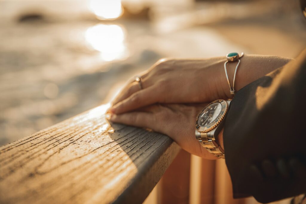 Hands resting on a wooden railing at sunset.