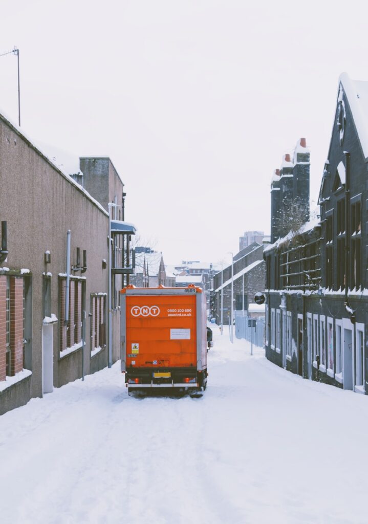 orange truck on snow covered road during daytime