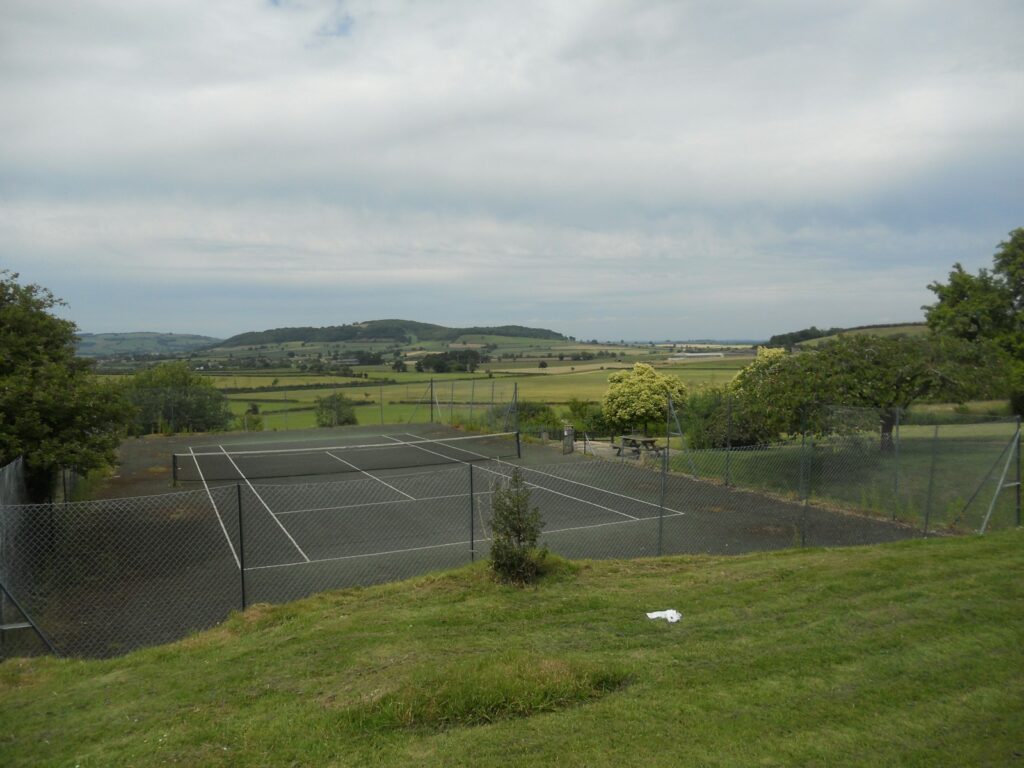 a tennis court surrounded by a lush green field