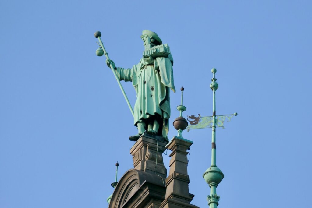 A weathered copper statue atop a building against blue sky
